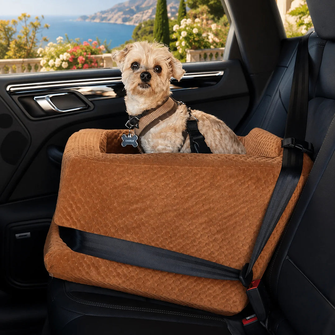 Animals Matter LA Dog Company Rider Turbo dog car seat  2X in saddle, featuring a small dog secured in a quilted car seat inside a car with a coastal view.